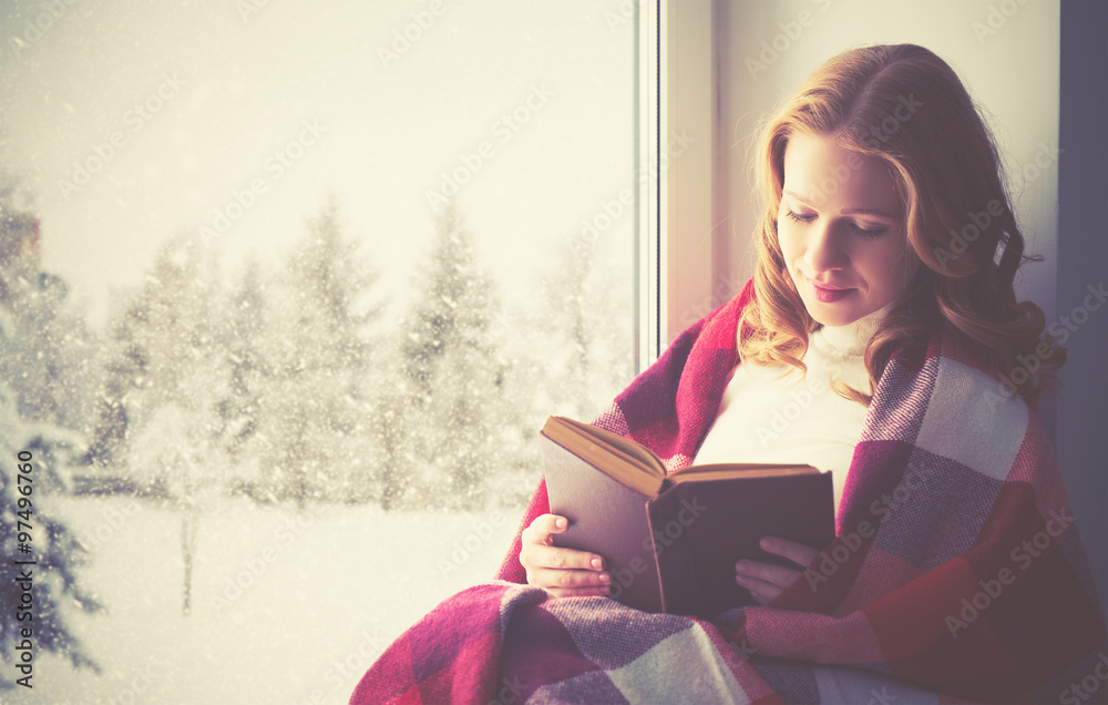 happy girl reading book by the window in winter