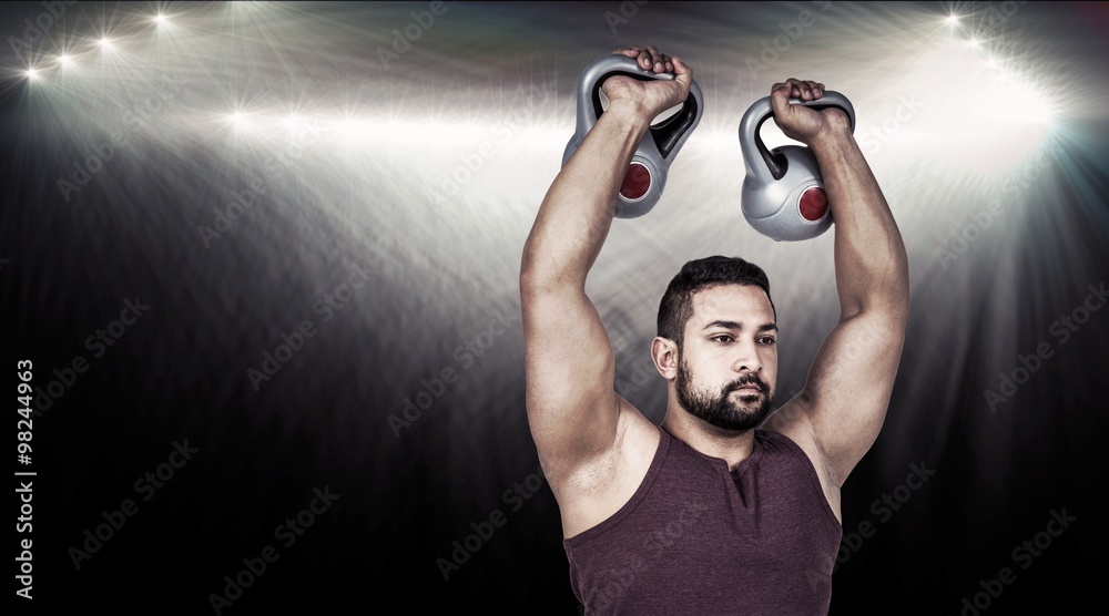 Composite image of muscular serious man lifting kettlebells