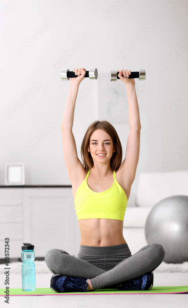 Beautiful young girl doing exercises with dumbbells at home