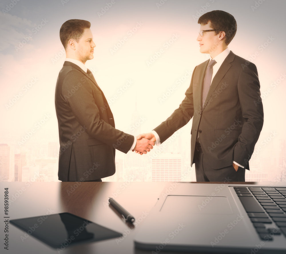 Businessmen shake hands and table withlaptop and digital tablet