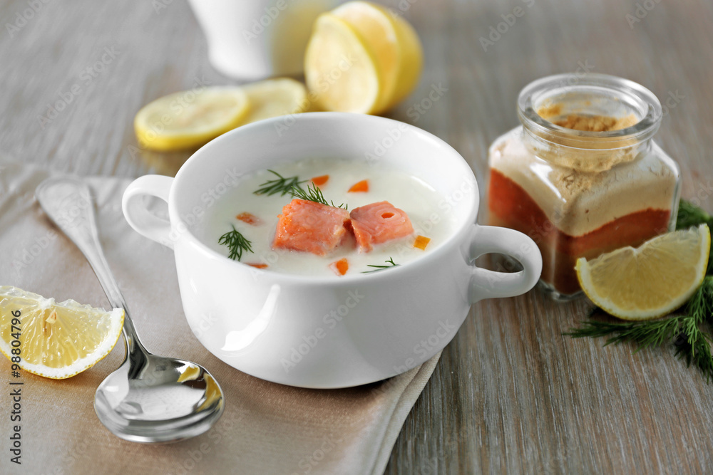 Delicious salmon cream soup on wooden table, which served with sliced lemon and spices