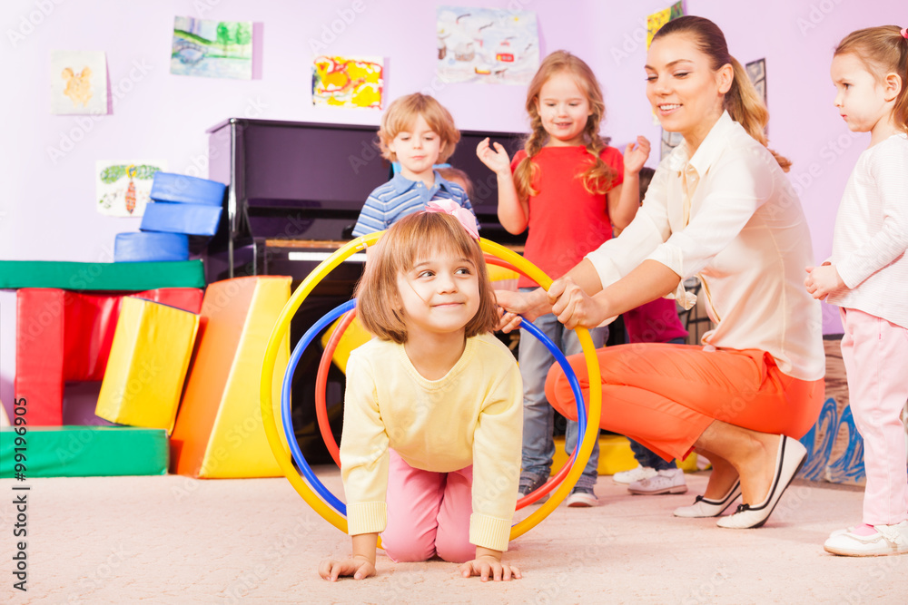 Girl crawl in plastic hoop, kindergarten group