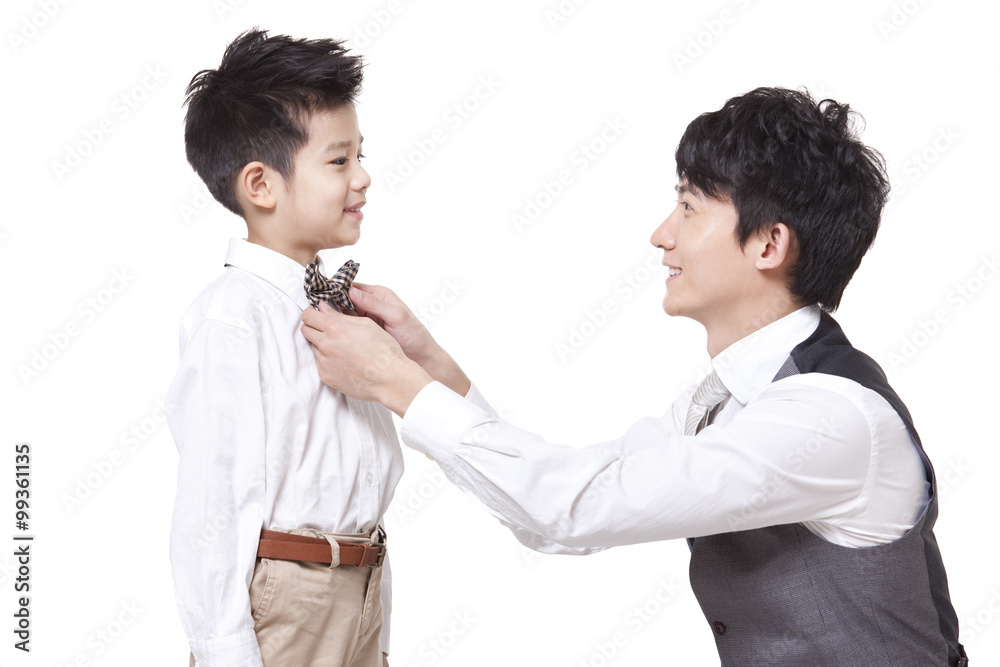 Smiling father fastening bow tie for son