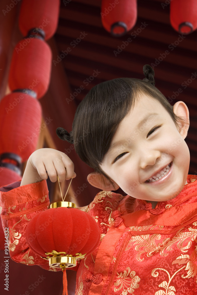 Young girl in festival Chinese New Year clothing, smiling at camera, holding Chinese lantern