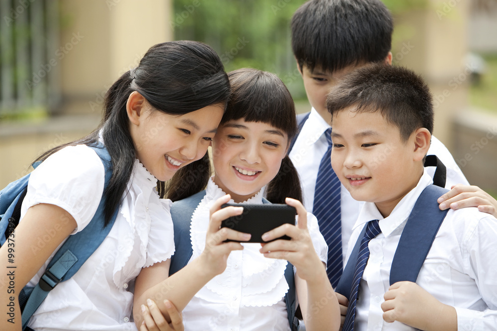 Excited schoolchildren in uniform with smart phone in school yard