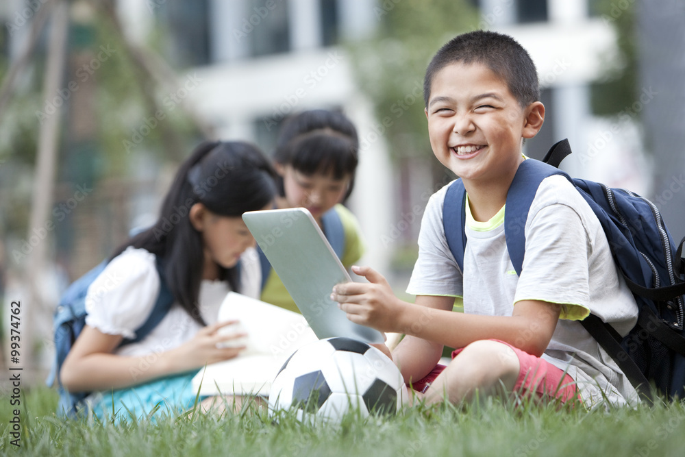 小学生拿着数字平板电脑坐在草坪上