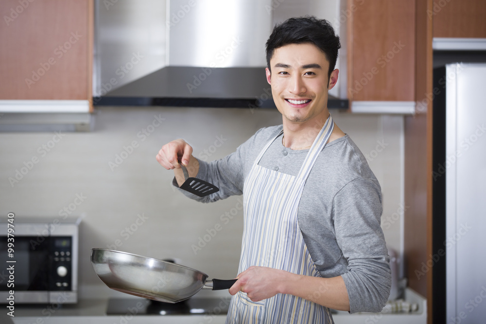 Cheerful young man cooking in kitchen