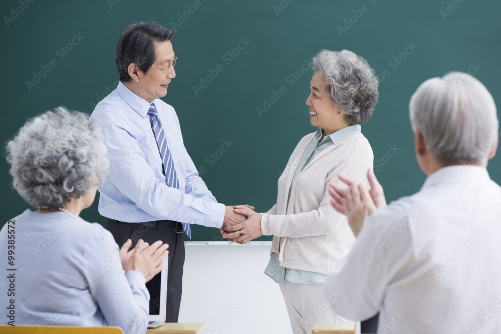 Senior student having a handshake with teacher in classroom