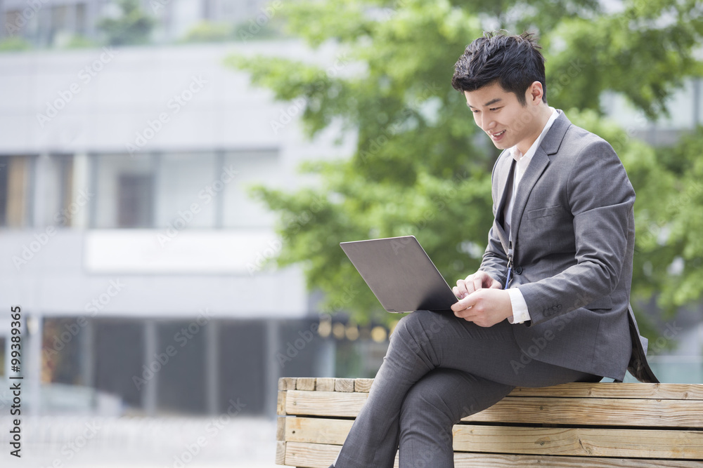 Young businessman working with laptop outdoors