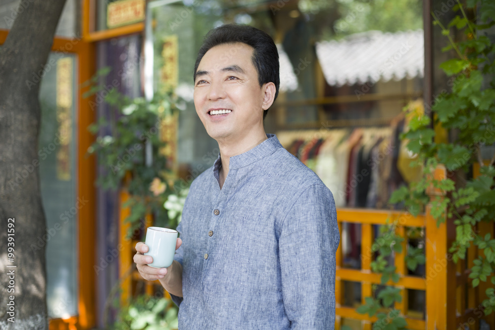 Male shopkeeper standing in doorway with a cup of tea