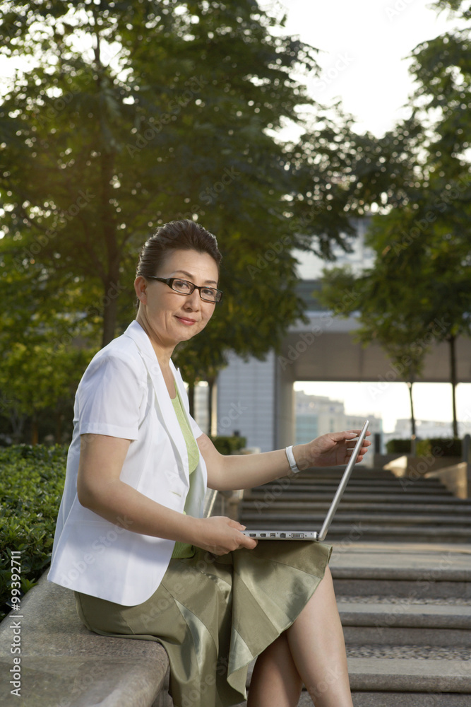 女商人坐在公园里使用笔记本电脑