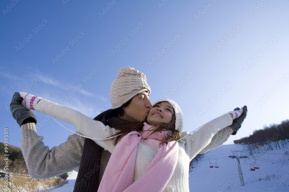 Young man kissing girls cheek with their arms outstretched