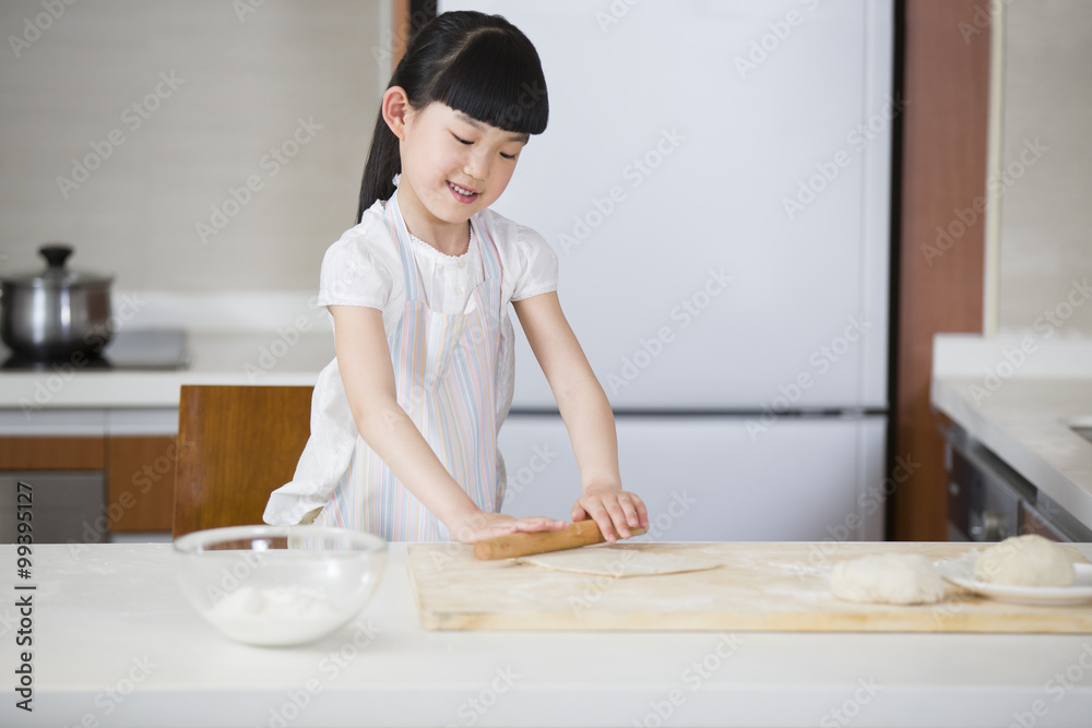 Smiling girl rolling dough with rolling pin on kitchen†worktop