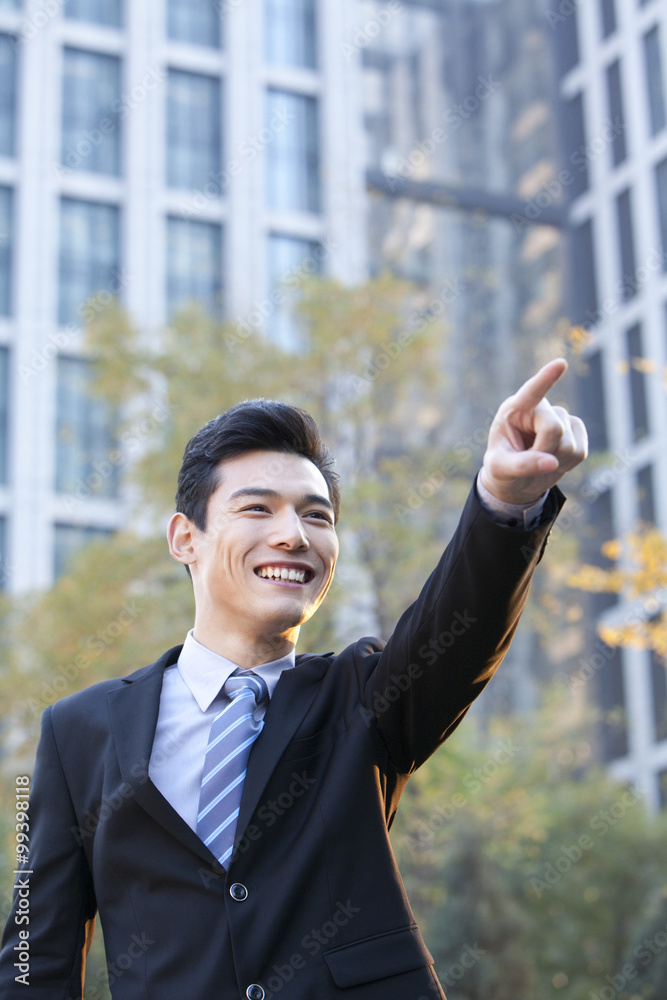 Businessman outside office buildings pointing to something