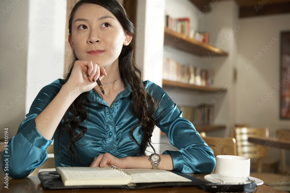 Woman Sitting At A Table With A Book Looking Contemplative