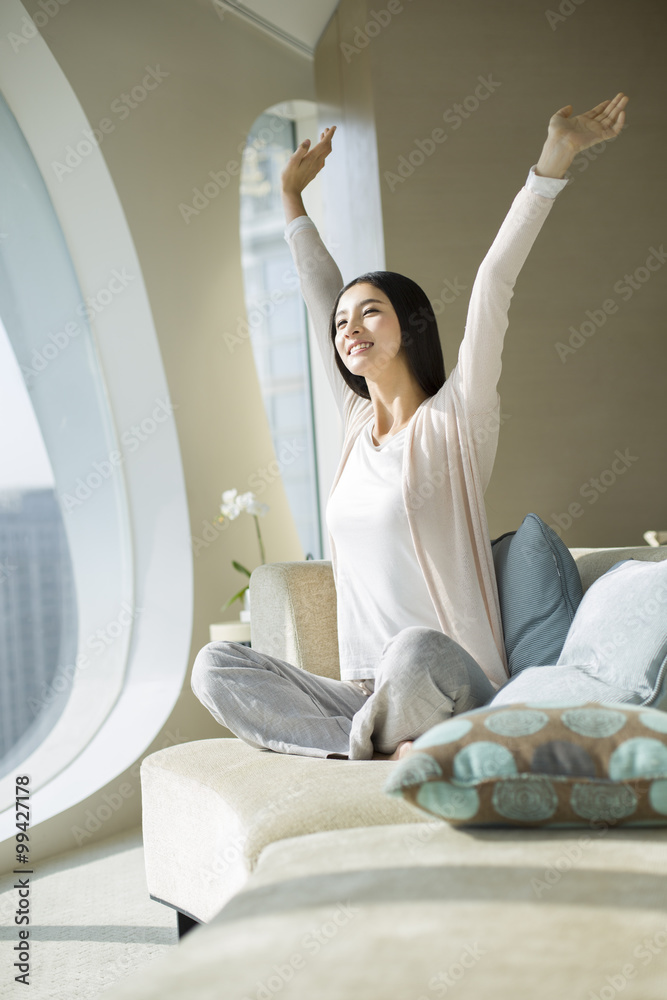 Happy young woman stretching arms on sofa