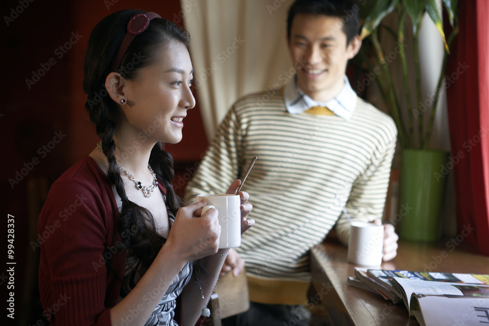 年轻男子和年轻女子端着咖啡杯在餐桌上