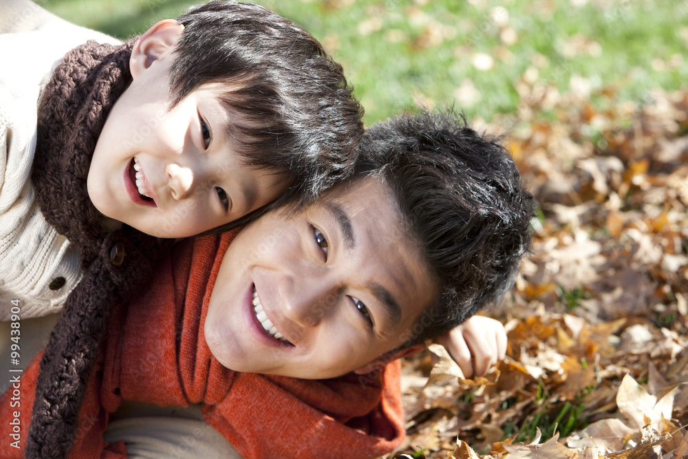 Father and son lying on the grass surrounded by Autumn leaves having fun