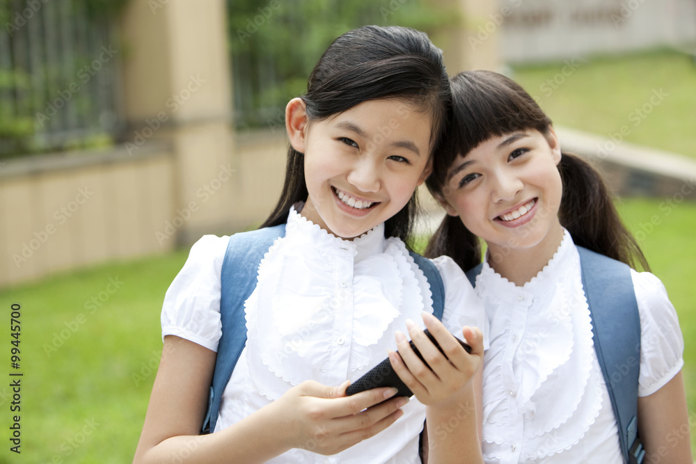 校园里穿着制服拿着智能手机的兴奋女学生