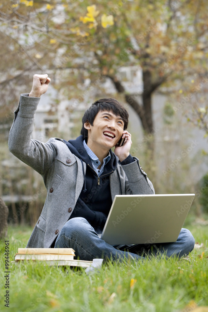 A young man raises arm in celebration while speaking on the phone