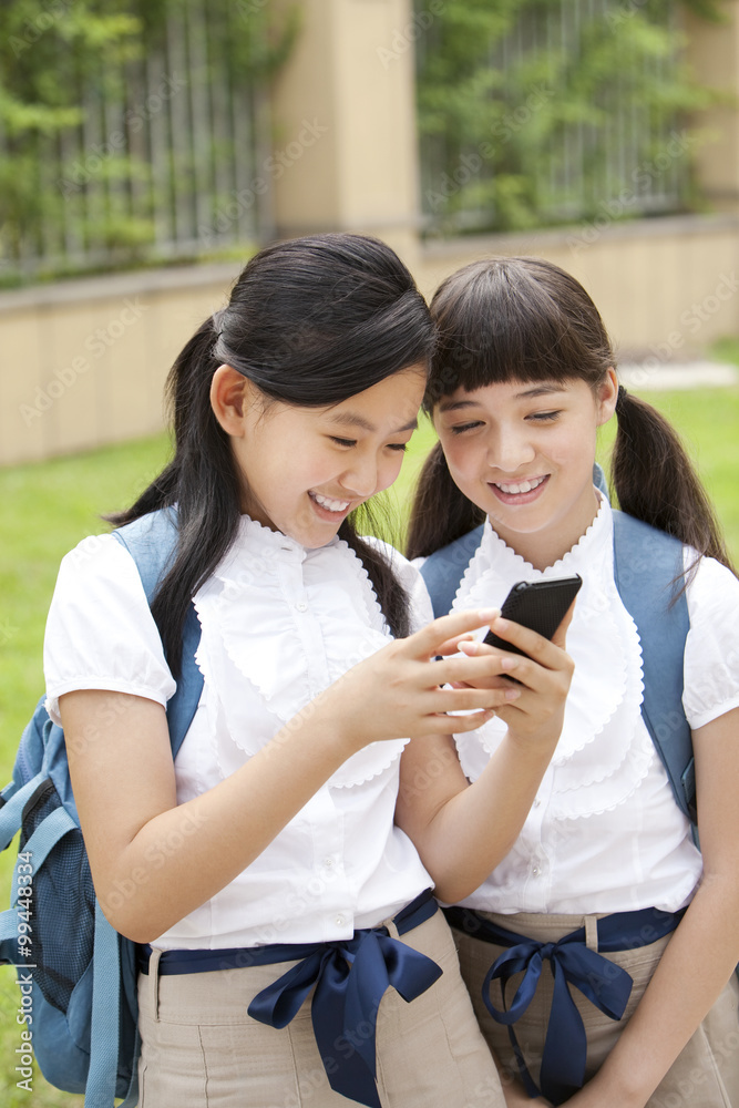 校园里穿着制服拿着智能手机的兴奋女学生