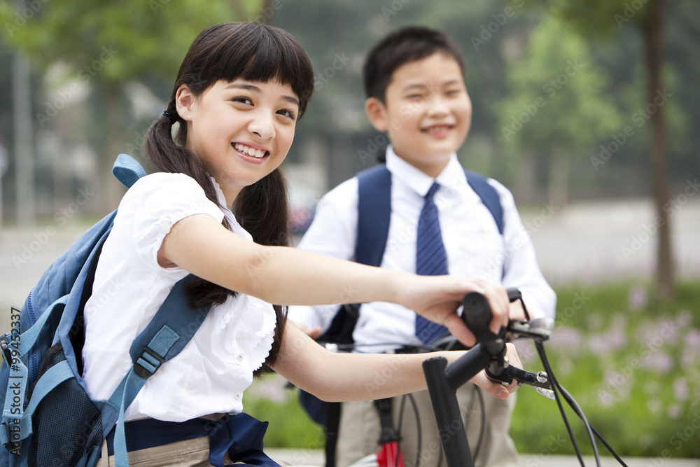 Happy schoolchildren in uniform with bicycles outdoors