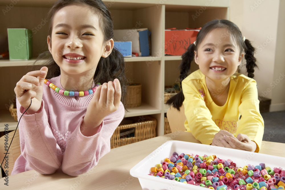 Girls Sitting In Classroom Smiling And Playing With Beads