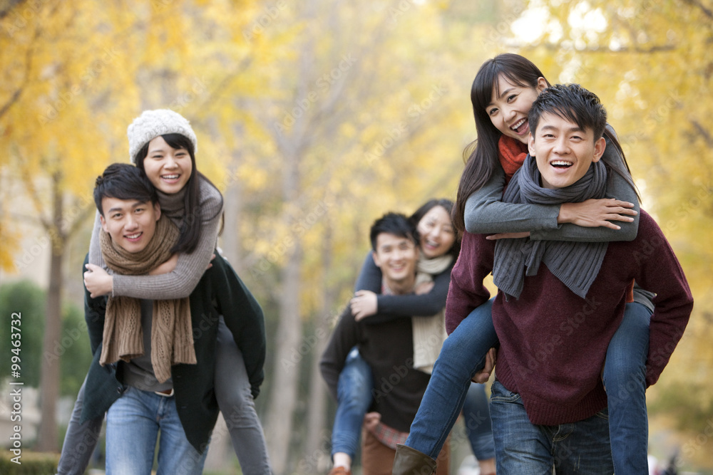 College students in pairs playing piggyback outdoors in autumn