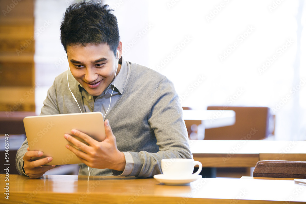 Young man enjoying videos in digital tablet in coffee shop