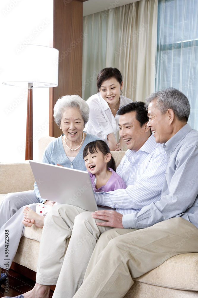 Grandparents and Parents with daughter look at Laptop on a sofa