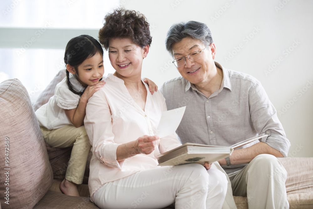 Happy grandparents and granddaughter looking at photo album