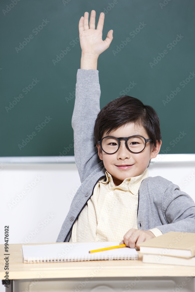 Happy schoolboy raising hand in classroom