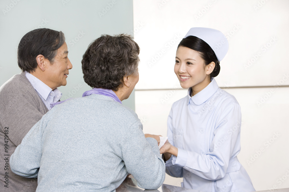 Young Nurse Helping Senior Couple at Nurses Station