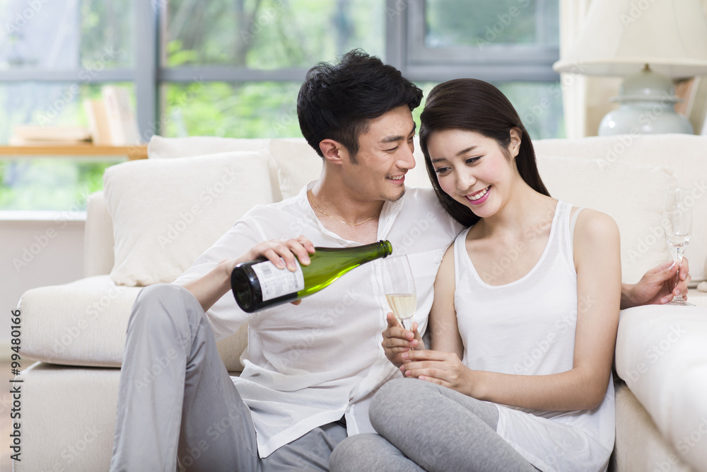 Cheerful young couple drinking champagne in living room