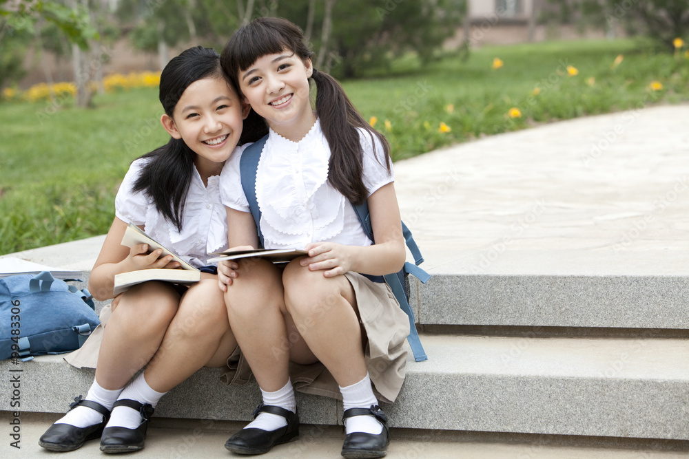 女学生拿着书坐在台阶上，在外面开心地笑着