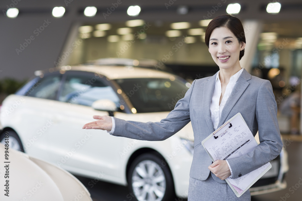 Confident saleswoman standing with new cars in showroom