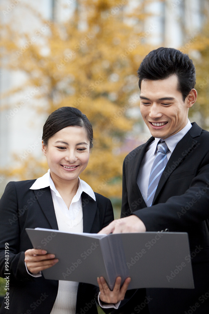 A businessman and businesswoman outside office buildings looking at a document