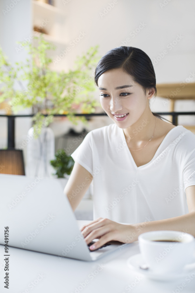 快乐的年轻女人在咖啡馆使用笔记本电脑