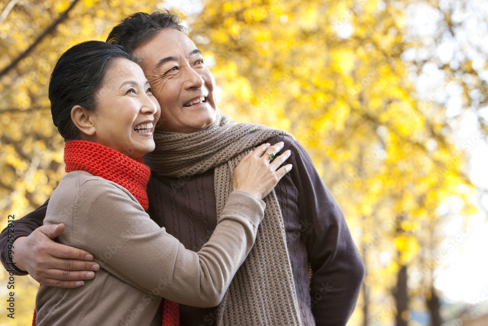 Senior couple embracing and surrounded by Autumn trees