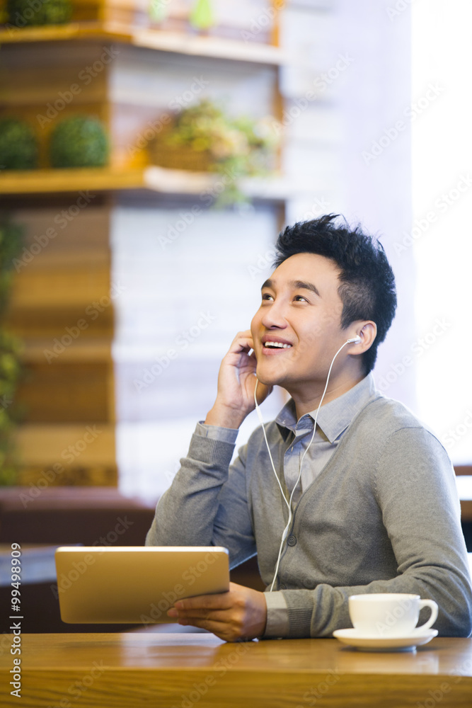 Young man enjoying music in digital tablet in coffee shop