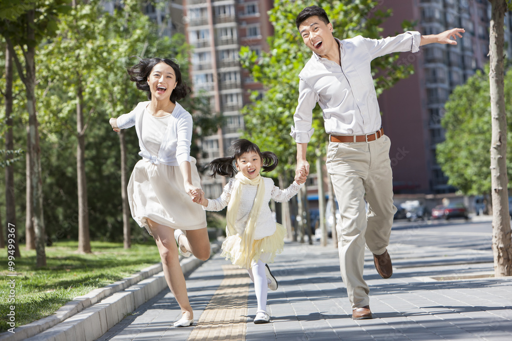 Excited young parents with daughter running on sidewalk hand in hand