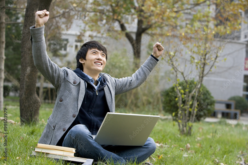 A young man raises arms in excitement on a grassy area