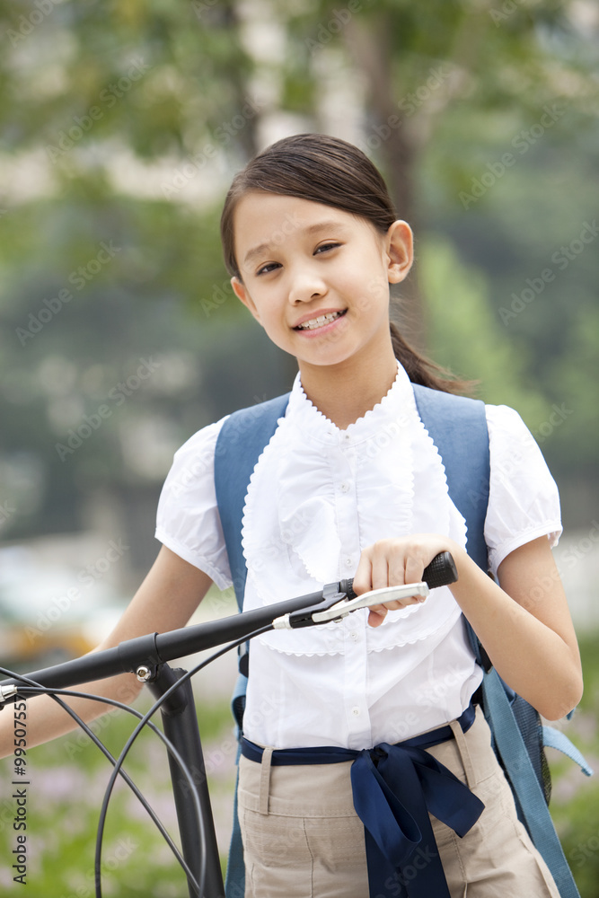 Happy schoolgirl in uniform with bicycle outdoors