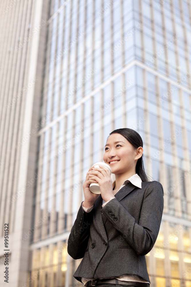 A businesswoman with a cup of coffee outside office buildings contemplating