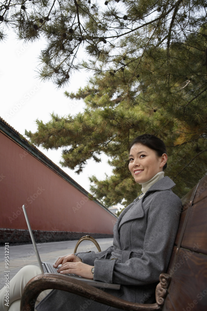 Businesswoman Sitting On A Park Bench Using Her Laptop Computer