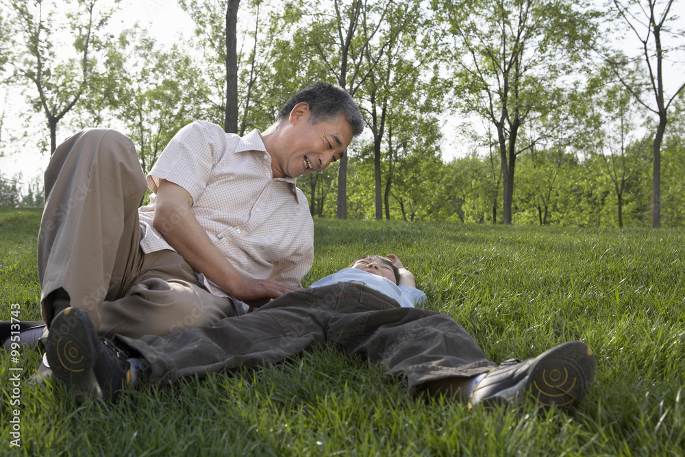 Grandfather And Grandson Laying In The Park