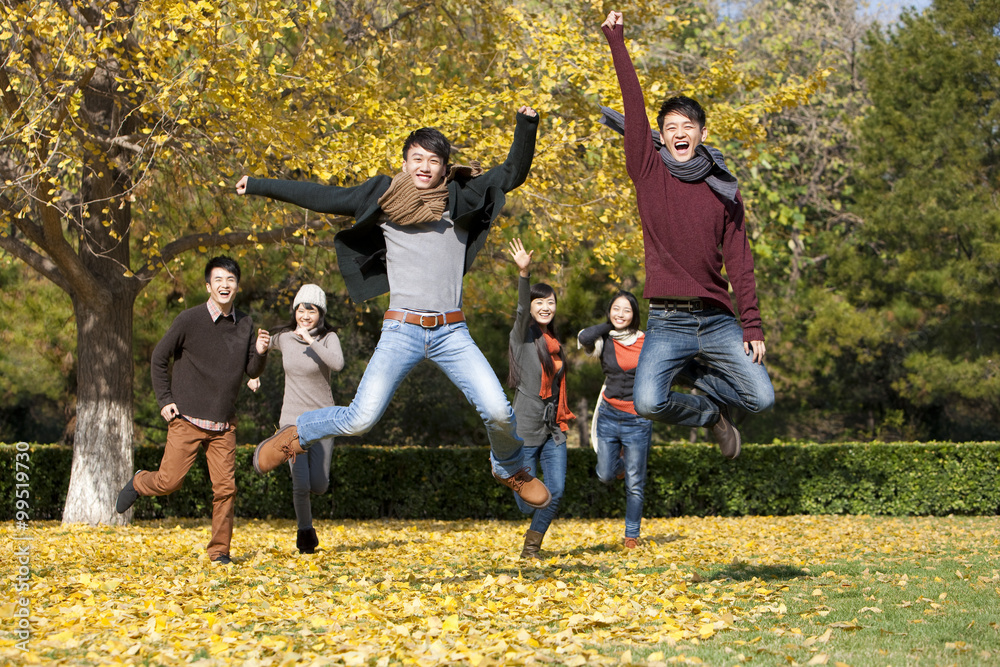 Excited young adults jumping on the lawn in autumn