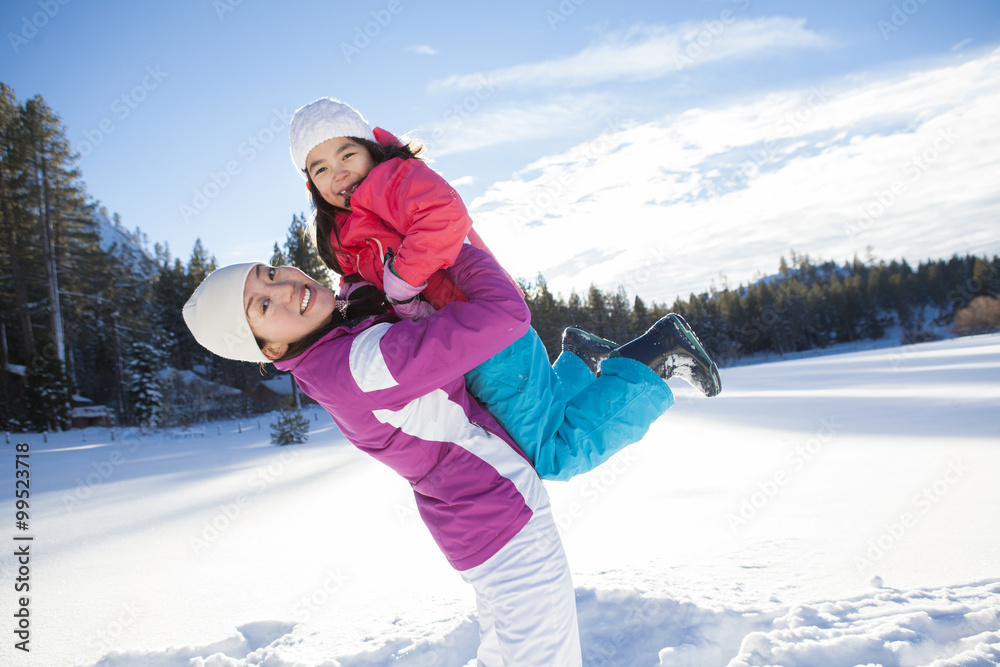 Mother holding daughter aloft on snow ground