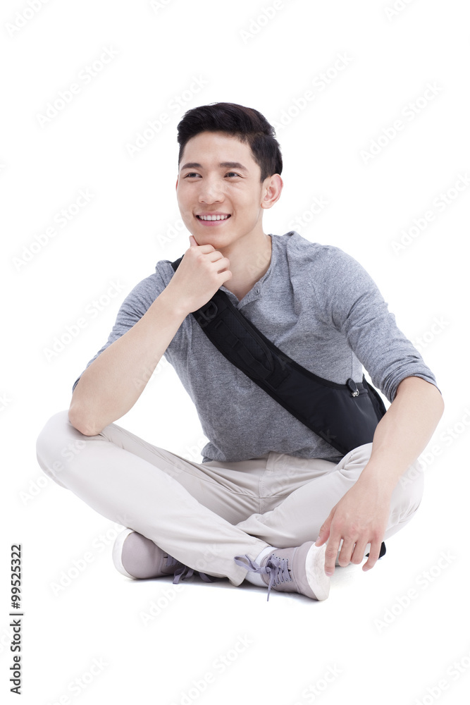 Happy male college student sitting cross-legged