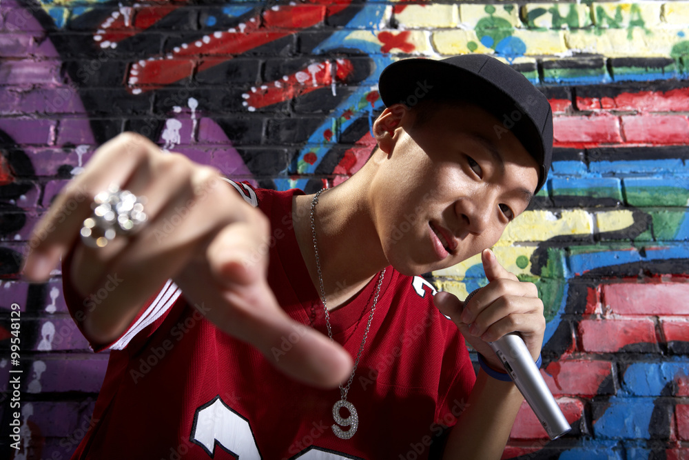 Teenage Boy Singing Into A Microphone In Front Of A Wall Of Graffiti